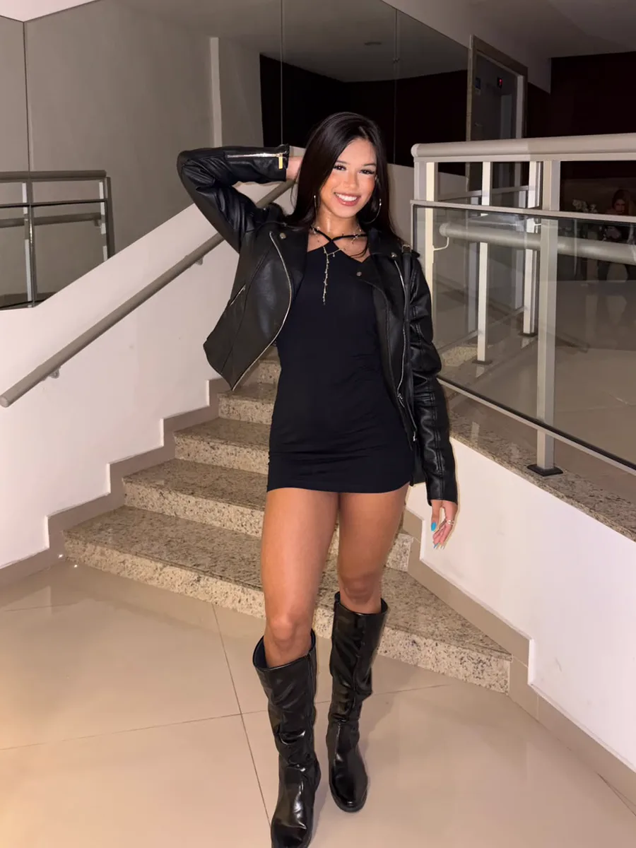 Ana, streamer da Fusion, de jaqueta de couro e vestido preto, sorrindo numa escada