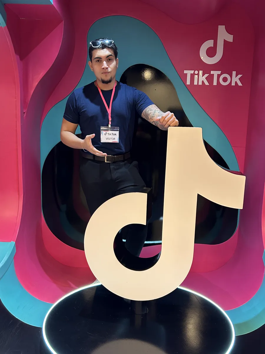 Yuri Rodrigues no escritório do TikTok, com crachá de visitante, ao lado do logo do TikTok